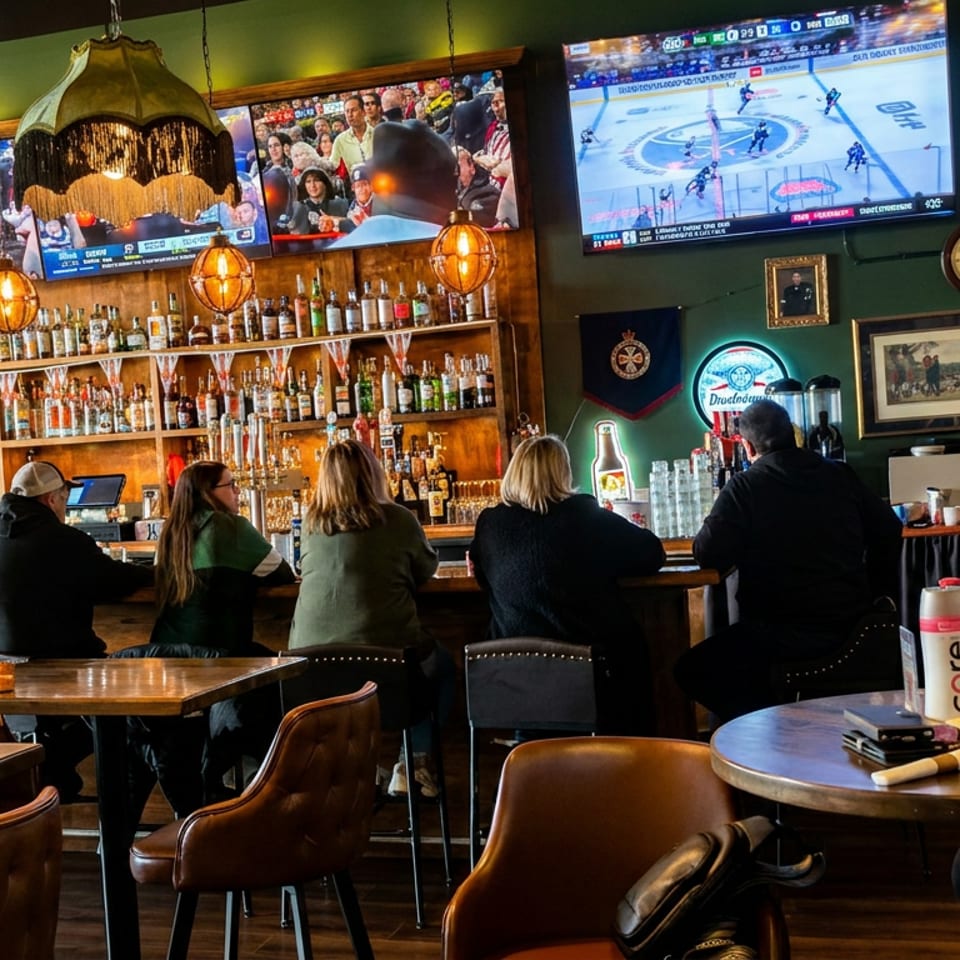 Sports bar interior with patrons at tables, a stocked liquor bar, pendant lights, and televisions showing soccer and hockey games.